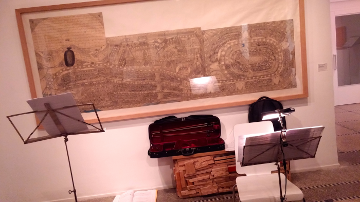 Dessin panoramique d’Adolf Wölfli accroché au mur du Musée Art & Marges, devant lequel sont disposés deux pupitres et un étui à violon ouvert